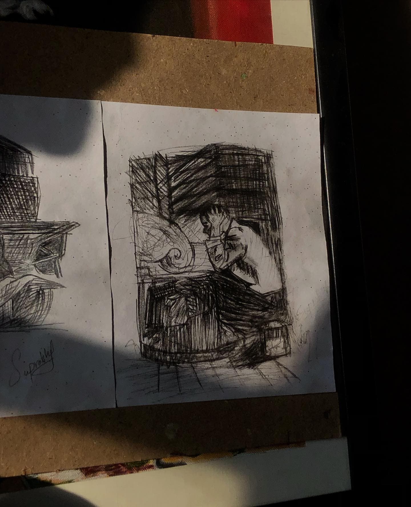 Dense black ink sketch of a figure holding their head inside compressed rooms, photographed under a hard desk shadow.
