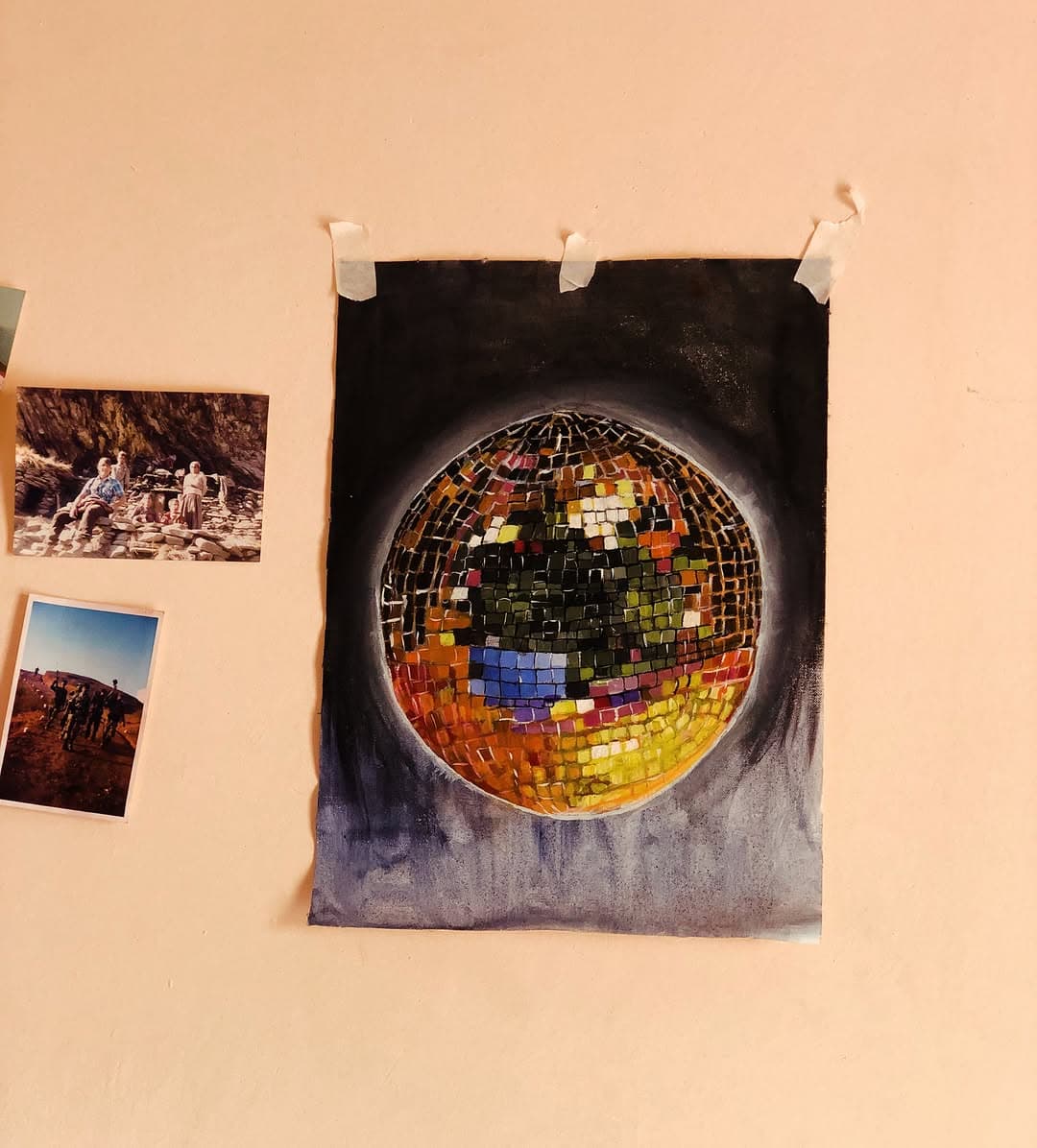 Colorful painted disco ball taped to a warm wall beside two small family photographs.