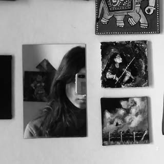 Black-and-white mirror portrait of Suprabha surrounded by artwork.